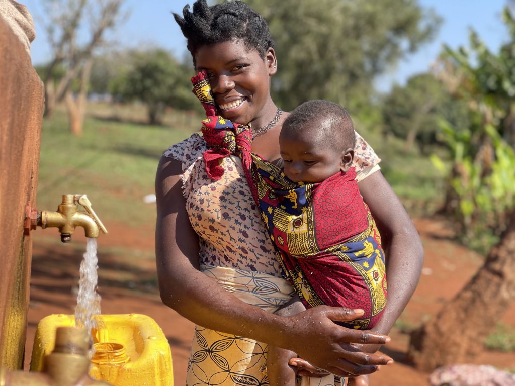Mother holding her child next to fresh pouring water