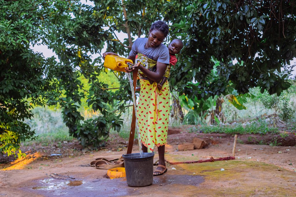 Mother with child on back pours water into bucket
