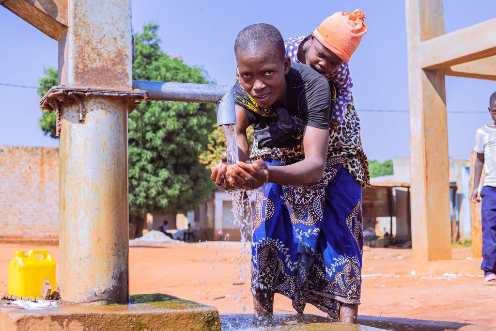 Woman with baby on her back holding hands under running water