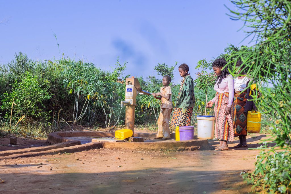 Young person pumping water while other community members wait