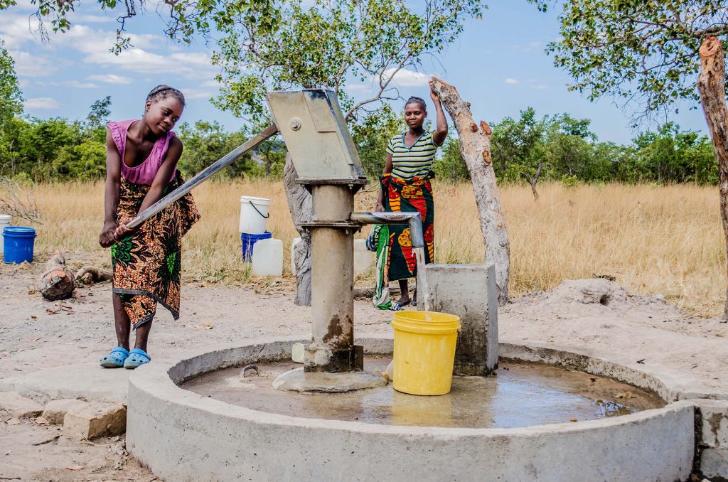 Young woman pumping fresh water while friend watches